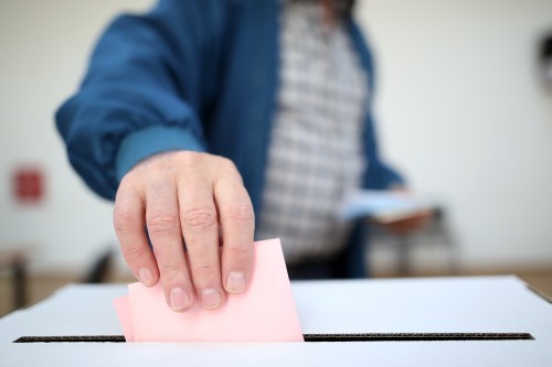 Das Bild zeigt eine Person, die einen Zettel in eine Wahlurne wirft.