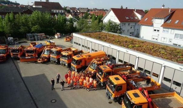 Hier ist ein Bild zu sehen: Ein großer Hof in dem 11 verschiedene Fahrzeuge stehen. Davor stehen die Fahrer der Fahrzeuge. 